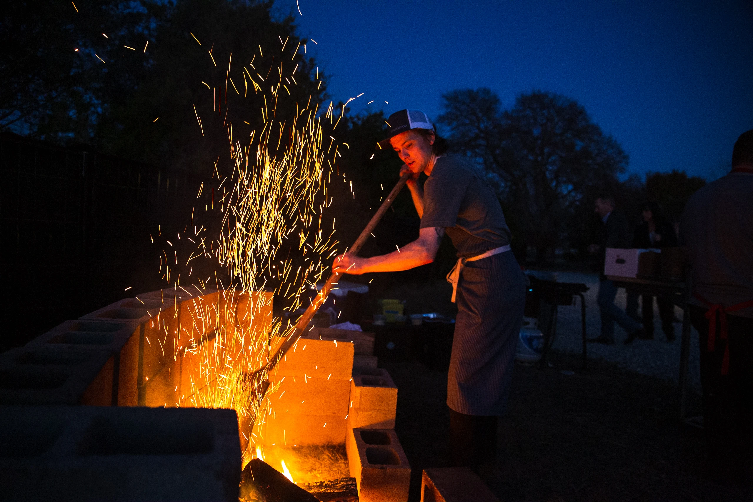 Sparks rising from an outdoor cooking fire against the evening sky.