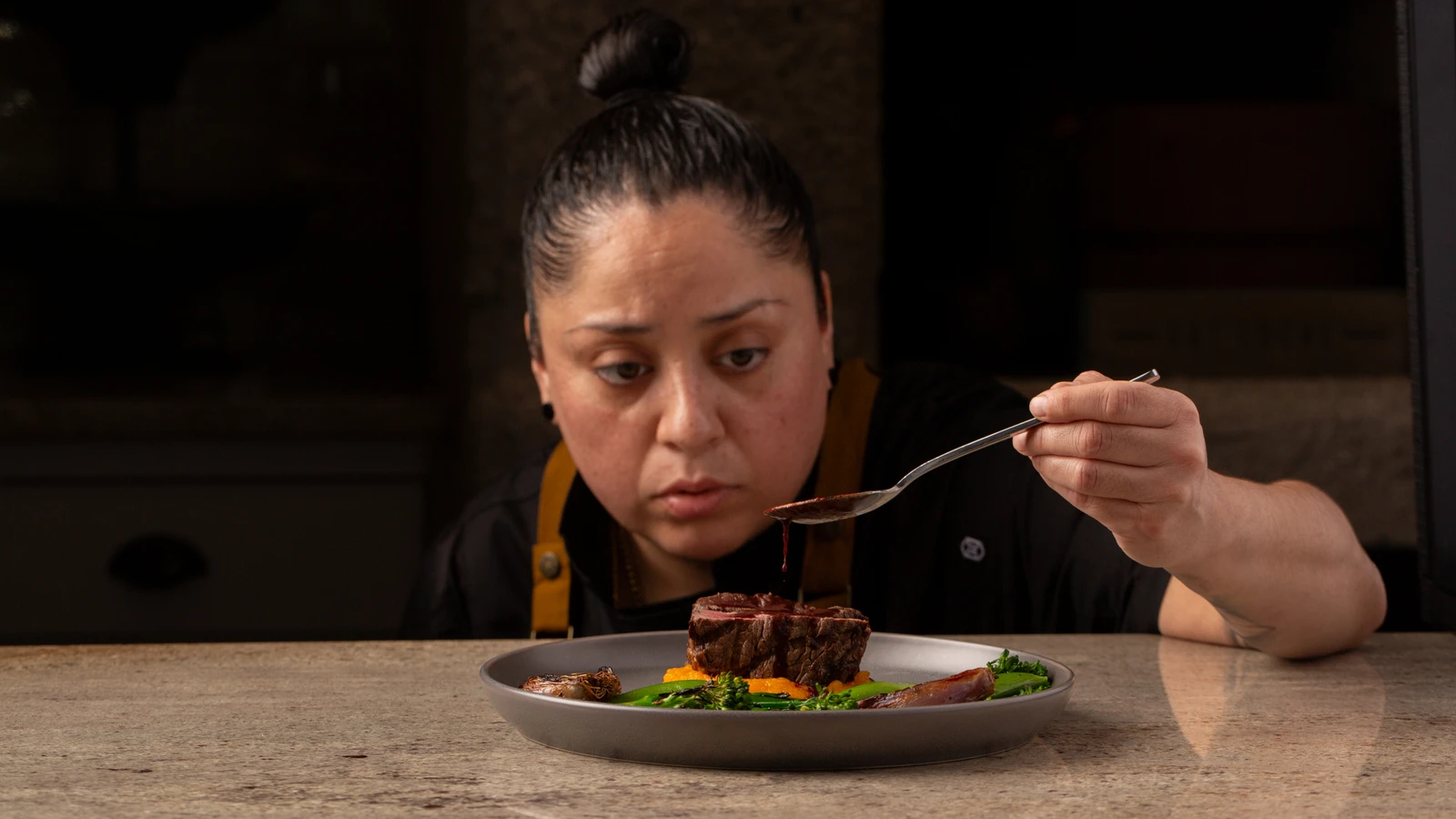 Chef Rosie Sanchez carefully spooning sauce over a finished dish.