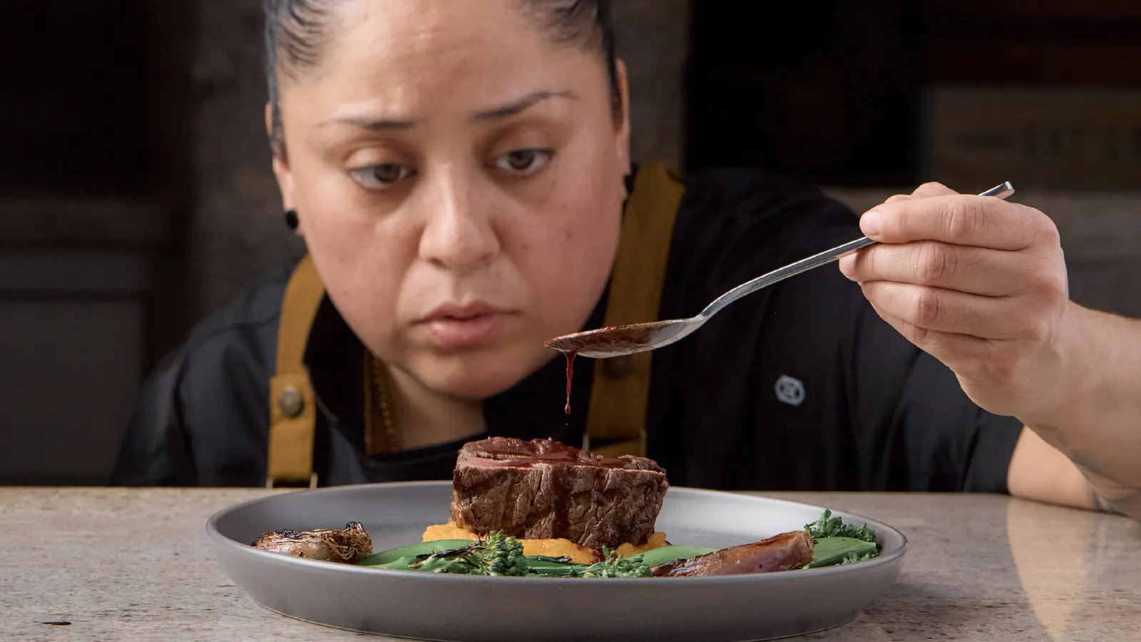 Chef Rosie Sanchez carefully spooning sauce over a finished dish.